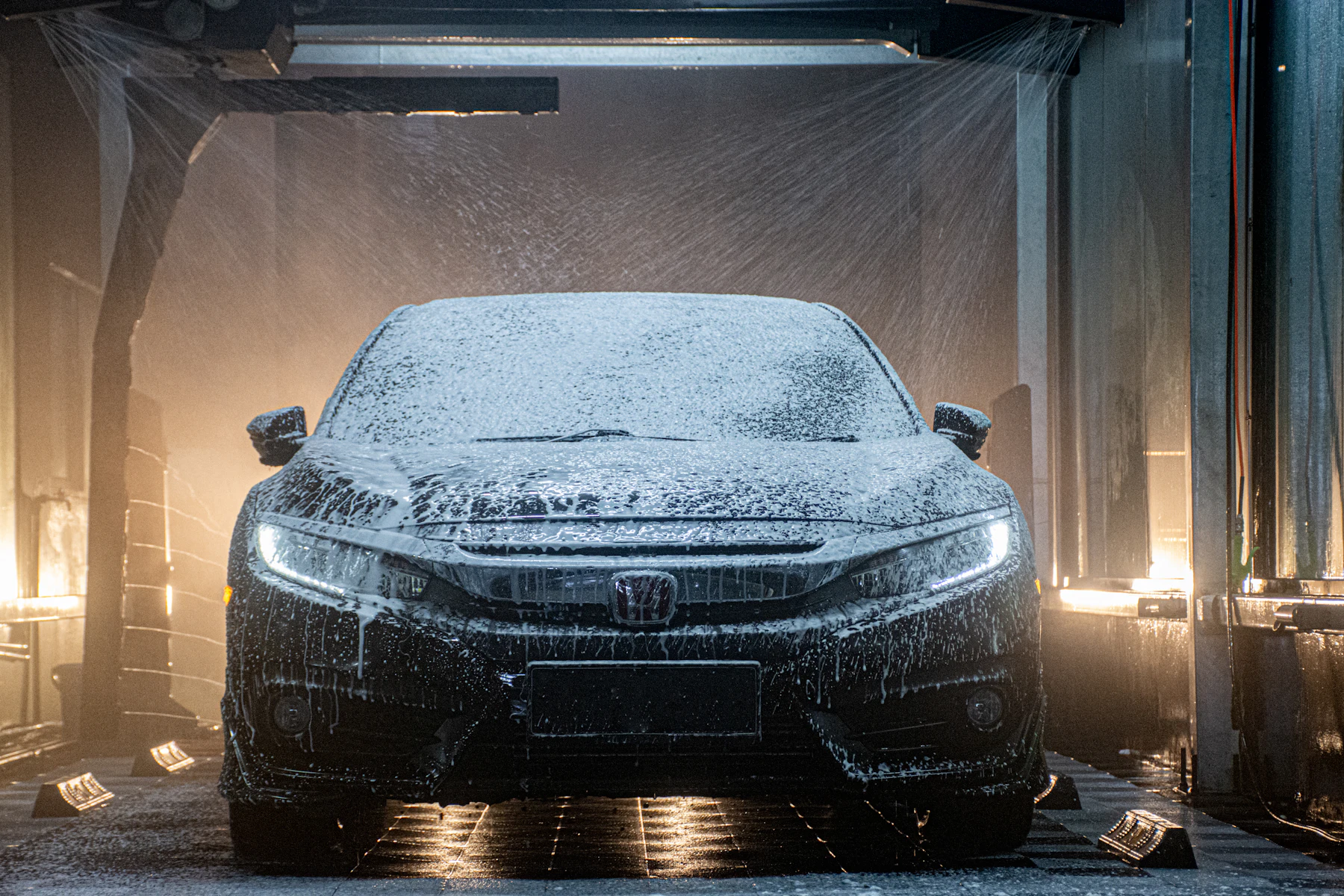 Car covered in foam inside a wash bay, headlights on