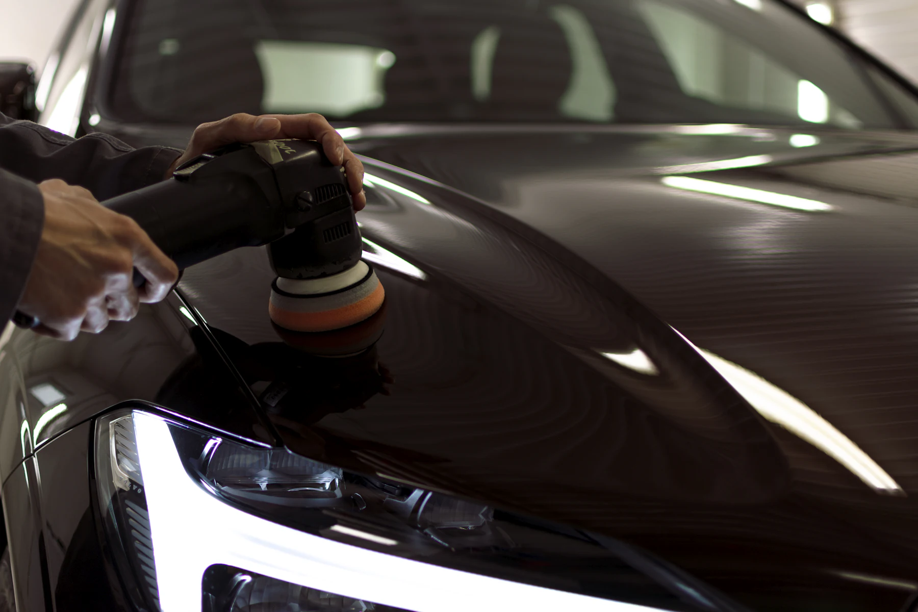 Detailer polishing a black car's bonnet